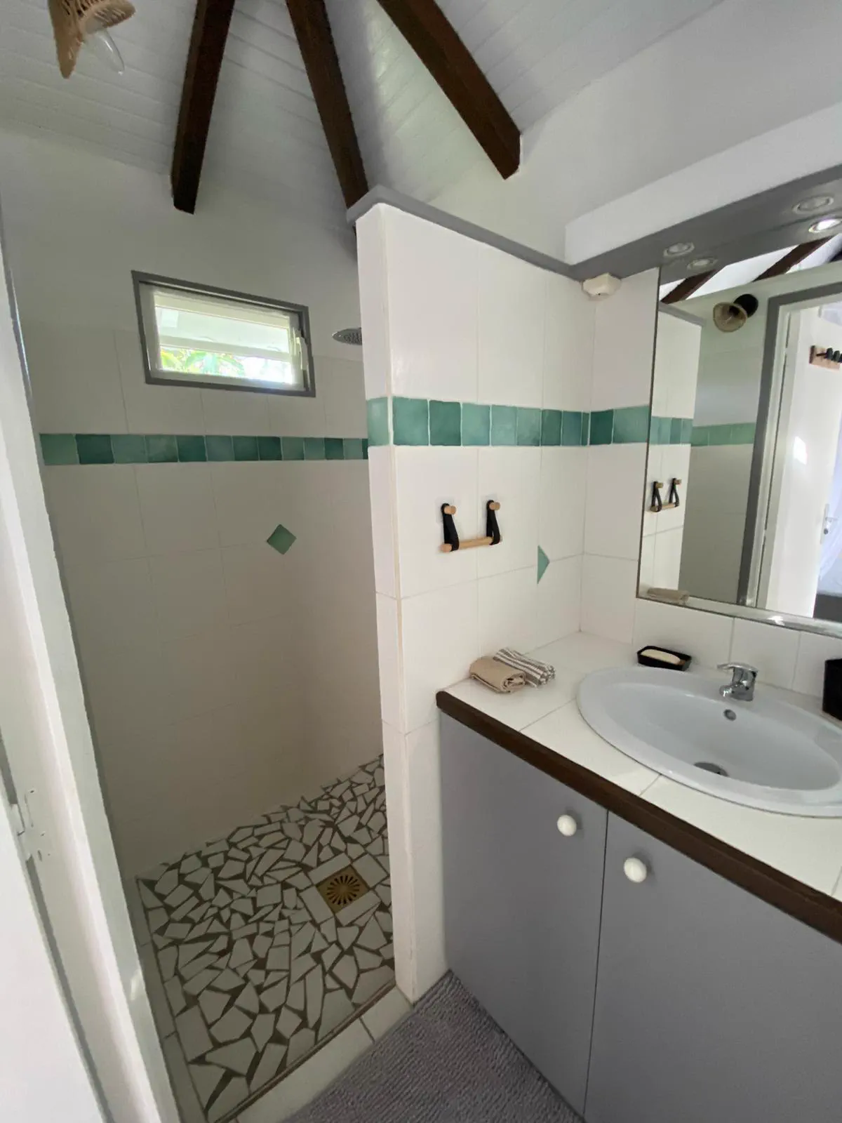La douche à l'italienne du bungalow, sol en galets, avec lavabo et miroir