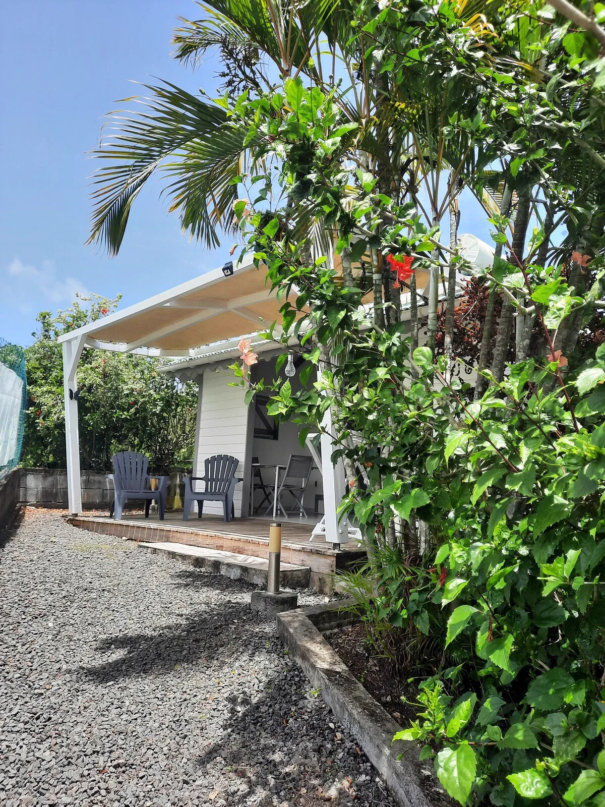Le bungalow Kaz Papillon et sa terrasse couverte, dans un jardin fleuri à Sainte-Anne