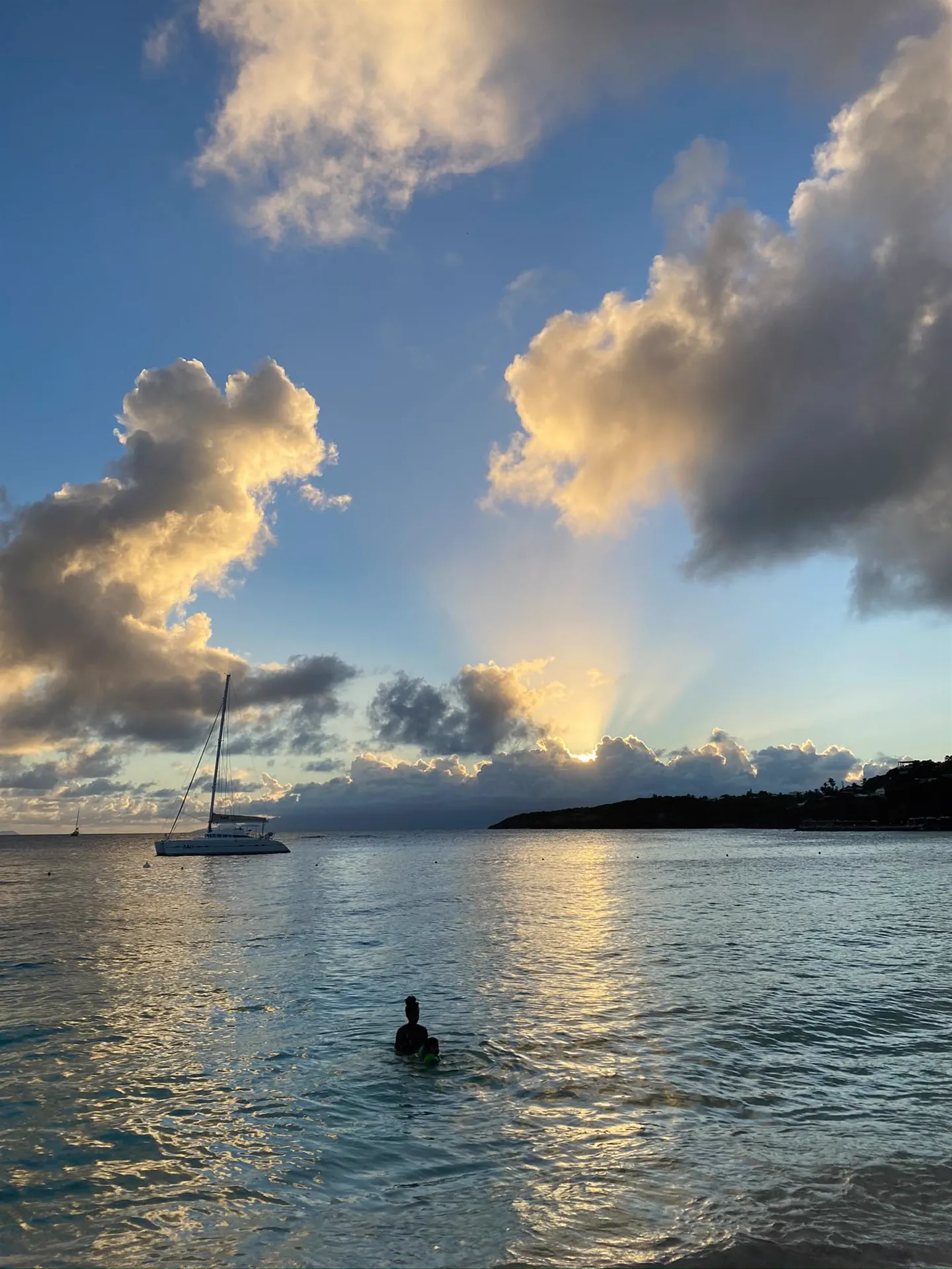 Le soleil bas derrière les nuages au-dessus de la mer, un catamaran au mouillage devant la plage de la Caravelle