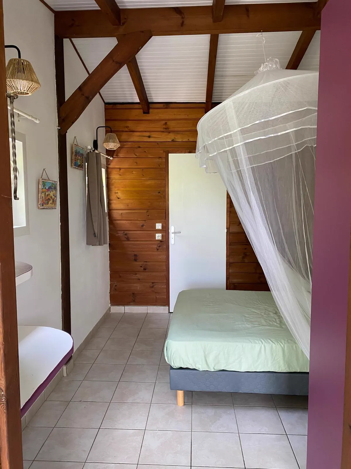 La chambre du studio : mur en bois, charpente apparente et lit sous moustiquaire